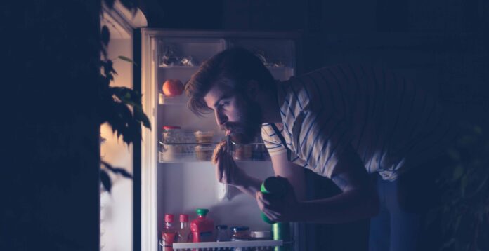 Man having snack and drinking beer late night in front of the refrigerator