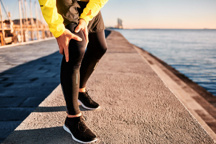 Knee Injury - sports running knee injuries on man. Close up of legs, muscle and knee outdoors. Male fitness athlete runner with pain from sprain knee.